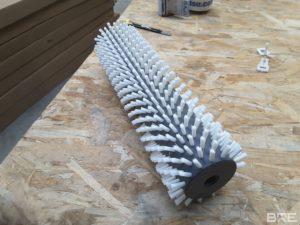 Une brosse rotative avec des soies rigides fixées sur un support cylindrique, conçue pour le nettoyage efficace des oignons en milieu industriel.