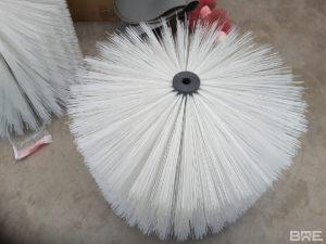 Une brosse rotative à garnissage long est présentée. Cette brosse est utilisée pour le transport automatisé de melons sur un convoyeur. Les poils longs de la brosse agrippent délicatement les melons et les font avancer sur le convoyeur.
