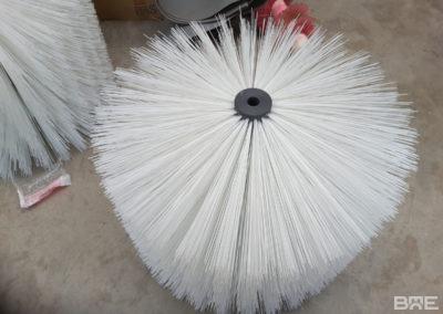 Une brosse rotative à garnissage long est présentée. Cette brosse est utilisée pour le transport automatisé de melons sur un convoyeur. Les poils longs de la brosse agrippent délicatement les melons et les font avancer sur le convoyeur.