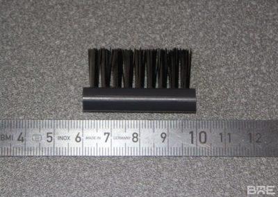 Une brosse d'étiqueteuse industrielle fixée sur un bras mécanique. Les poils en nylon souples de la brosse retiennent l'étiquette pendant l'échenillage pour un placement précis et une application uniforme.