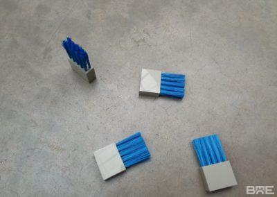 Une brosse industrielle en fibres synthétiques fixée sur un support métallique, utilisée pour le pressage et le lissage des étiquettes sur des produits dans une chaîne d'étiquetage industrielle.